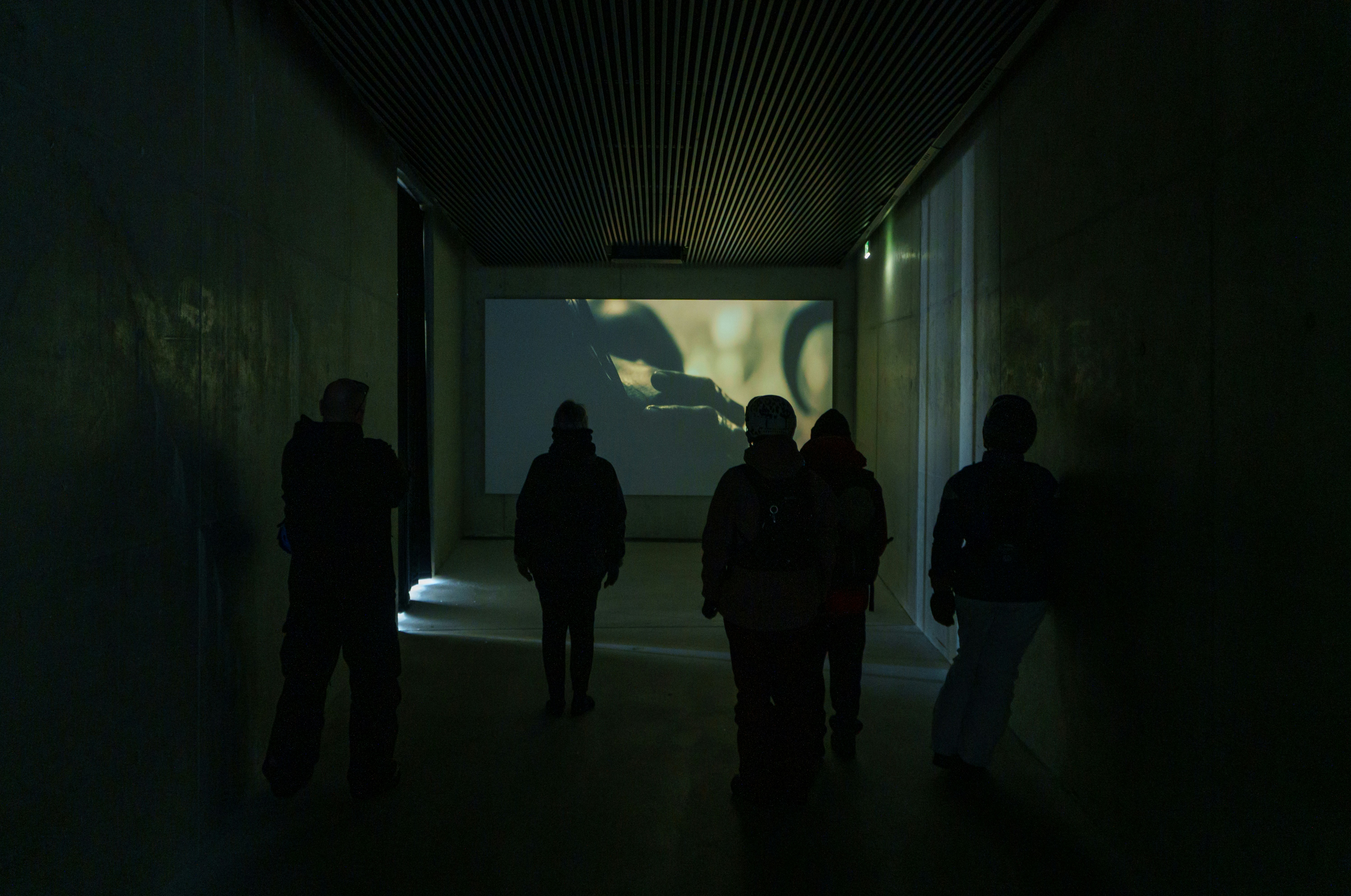 people standing around watching a projection of a film in a dark room